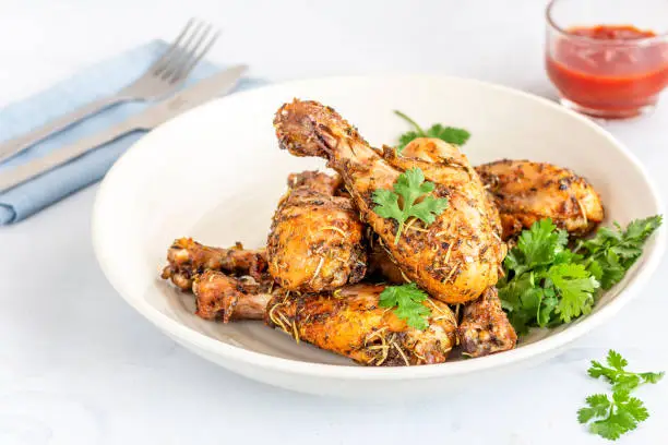 Baked Chicken Drumsticks with Tomato Ketchup and Cilantro on a White Background, High Angle Photo.