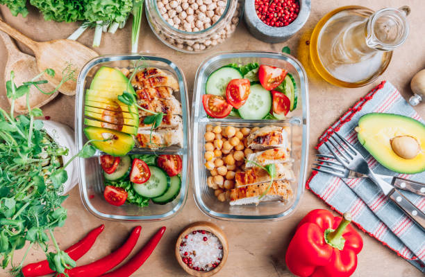 recipientes de preparación de comidas saludables con garbanzos, pollo, tomates, pepinos y aguacates. almuerzo saludable en envases de cristal sobre fondo rústico beige. concepto de cero residuos. enfoque selectivo. - preparar comida fotografías e imágenes de stock