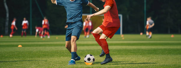 due uomini che calciano pallone da calcio. junior teenage soccer team in allenamento.  atleti che corrono con palla sul campo di calcio. giovani calciatori in azione - lega di calcio foto e immagini stock