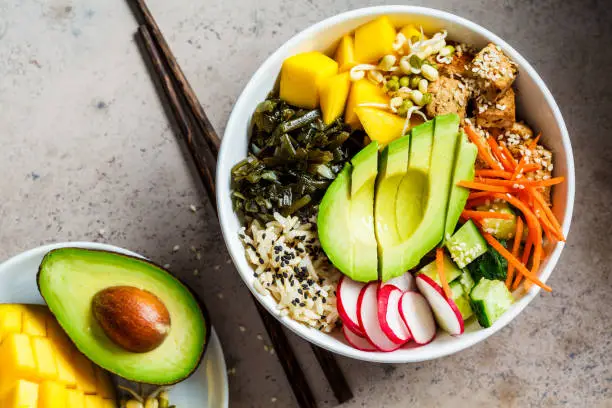 Vegan poke bowl with avocado, tofu, rice, seaweed, carrots and mangoes. Vegan food concept.