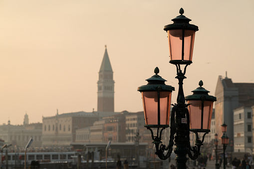 Old street lamp shining on empty waterfront with gondolas parking in Grand Canal in Venice, facing opposite side with Campanile di San Giorgio on quiet evening, long exposure shot