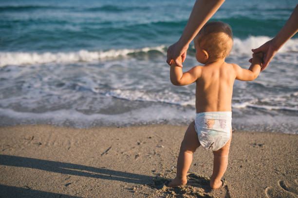 istock mom helps to make the child's first steps on the beach 1205567316