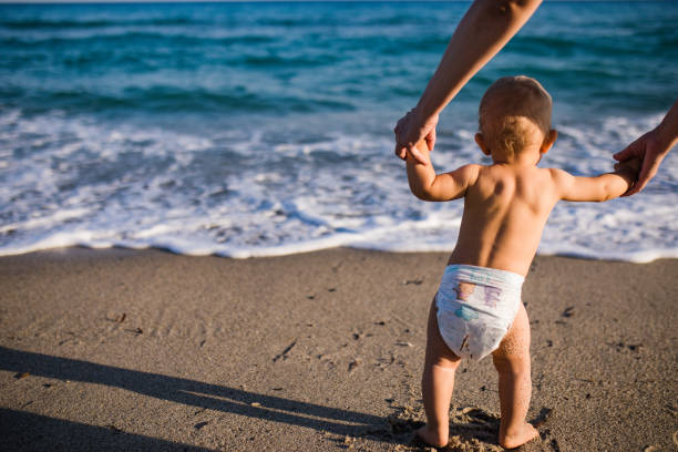 istock mom helps to make the child's first steps on the beach 1205568214