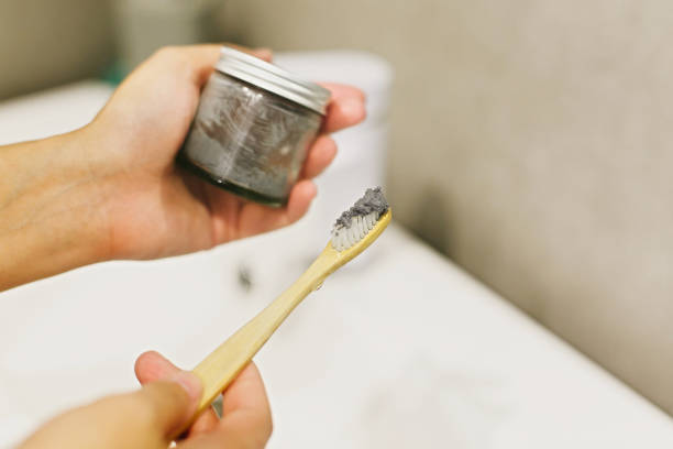 istock Zero waste bathroom concept. Woman using bamboo toothbrush and charcoal toothpaste from glass jar for daily cleaning routine. Recycle and reuse. Wooden toothbrush with paste closeup 1205572418