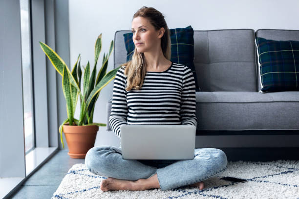 istock Pretty young woman looking through the window while using her laptop at home. 1205572619