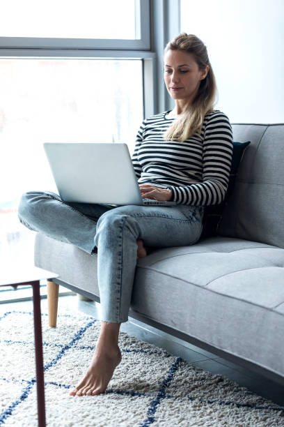istock Pretty young woman using her laptop while sitting on sofa at home. 1205573289