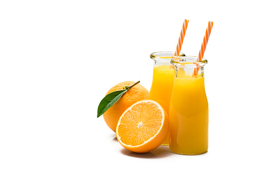 Front view of two orange juice bottles shot on reflective white background. Drinking straws are in the bottles. Whole and sliced range fruits are beside the bottles. The composition is at the right of an horizontal frame leaving useful copy space for text and/or logo at the left. Predominant colors are orange and white. High resolution 42Mp studio digital capture taken with Sony A7rii and Sony FE 90mm f2.8 macro G OSS lens