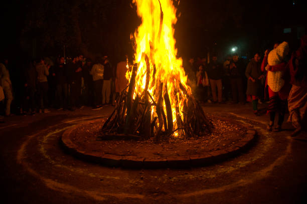 Giant bon fire lit for the festival of Lohri surrounded by people Gurgaon, India, Circa 2020 - Photograph of a giant bonfire lit for the auspicious festival of lohri or Holi or Holika Dahan. The fire is surrounded by people enjoying the festival. This is a spring harvest festival celebrated in India by roasting grain, popcorn, sesame seeds, chikki, peanuts and collecting coal fire natural phenomenon photos stock pictures, royalty-free photos & images