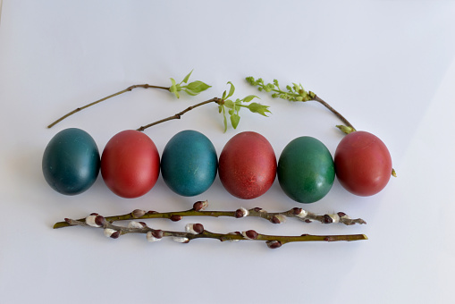 Easter eggs of various colors, willow branches lie in one row.