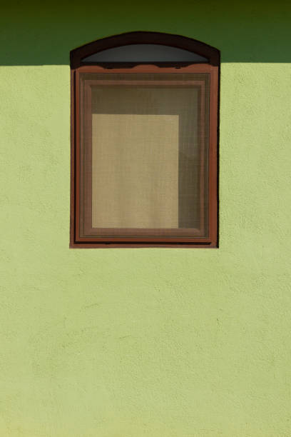 Curtained brown window on a green textured wall with a mosquito net in the sunlight..