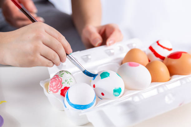 Cute gently child hands painting Easter eggs. The mother helps her son paint an egg with a paintbrush at home. Happy family preparing for Easter. Close up, selective focus
