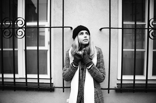 December 4th, 2019 - Warsaw, Poland: pretty young Ukrainian woman in coat and turtleneck sweater standing and leaning to a wall in old town, black and white photo