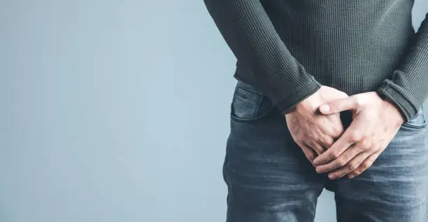 Man holding his urethra in pain on gray background