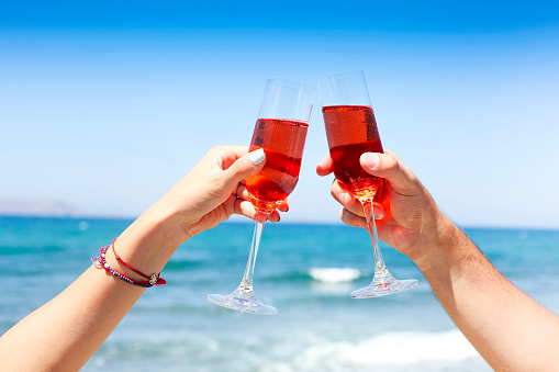 Hands of couple enjoying glasses of champagne on tropical beach in sunny summer day