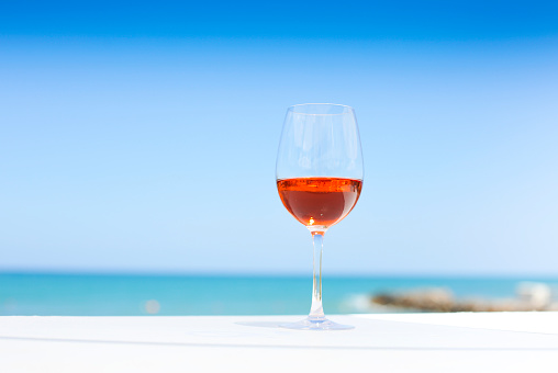 Glass of rose wine against blue water and sea in summer day