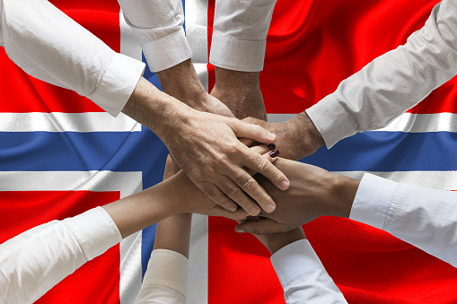 group of people joining hands over waving norwegian flag