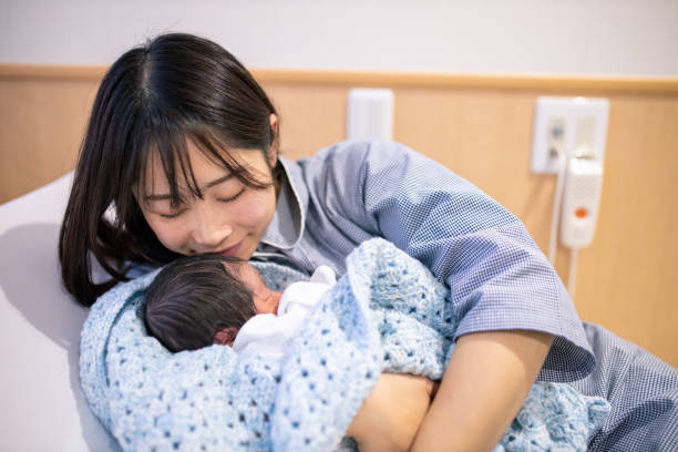 молодая мать держит своего нового ребенка и целуется в больнице - mother baby new kissing стоковые фото и изображения