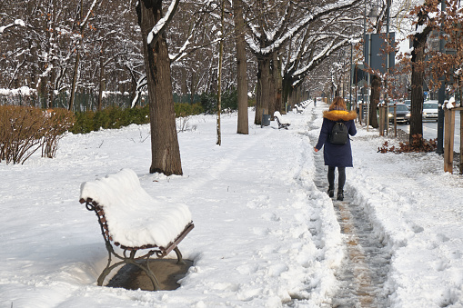 Bucharest, Romania - February 6, 2020: Woman walks on a narrow, slippery footpath, made by pedestrians on a snow covered sidewalk, many hours after the first snow of a mild Winter in Bucharest.