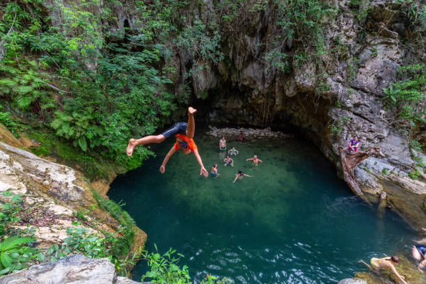 People enjoying a beautiful water pond by the waterfall in a canyon. Trinidad, Cuba - June 12, 2019: People enjoying and cliff jumping in a water pond by the waterfall in a canyon. cliff jumping stock pictures, royalty-free photos & images