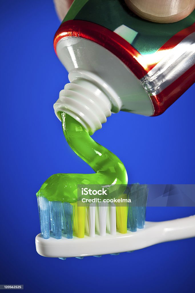 toothpaste being squeezed onto a toothbrush toothpaste being squeezed onto a toothbrush on a dark blue background Blue Stock Photo