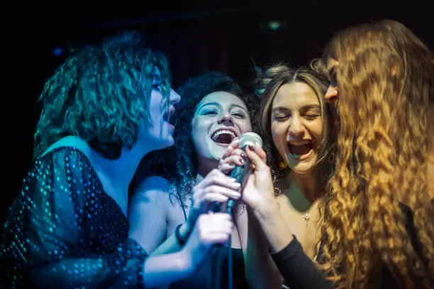 Girls are smiling dancing singing and enjoying the night at karaoke party