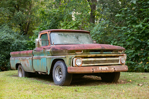 An old rusty Chevrolet truck sitting in a grass field with trees in the background.