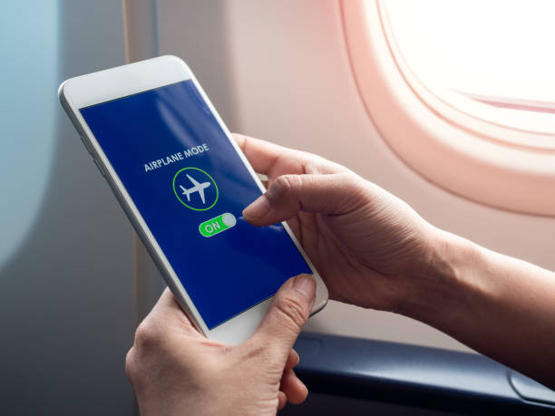 istock Flight mode concept. Hand holding white smartphone and turned on airplane mode on screen near the window on the airplane. 1205659444