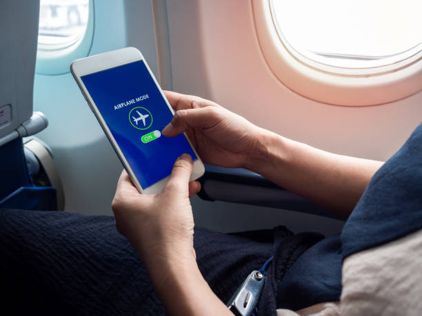 Flight mode concept. Hand holding white smartphone and turned on airplane mode on screen near the window on the airplane. Flight mode concept. Hand holding white smartphone and turned on airplane mode on screen near the window on the airplane. aboard stock pictures, royalty-free photos & images