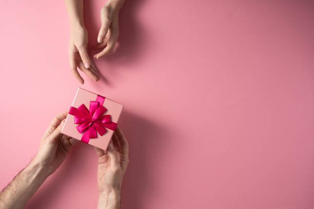 istock Valentine's Day celebration concept. A nice gift from a loved one. Box with a bow hands of a man and a woman on a delicate pink background. Copy space. Flat lay. 1205662374