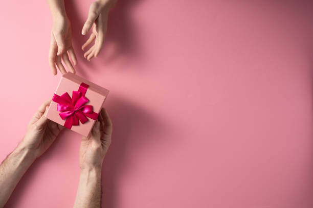 istock Valentine's Day celebration concept. A nice gift from a loved one. Box with a bow hands of a man and a woman on a delicate pink background. Copy space. Flat lay. 1205662388