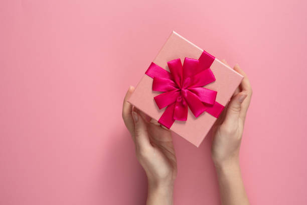 istock Valentine's Day celebration concept. A nice gift from a loved one. Box with a bow in female hands on a delicate pink background. Copy space. Flat lay. 1205662406