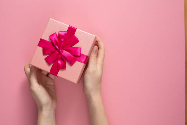 istock Valentine's Day celebration concept. A nice gift from a loved one. Box with a bow in female hands on a delicate pink background. Copy space. Flat lay. 1205662432