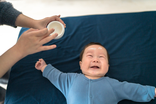 Applying moisturizing cream on face of baby