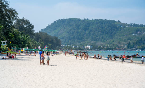 Aerial summer view of Patong Beach in Phuket, Thailand. People are walking along the beach, swimming or laying down resting on the white sand beach.