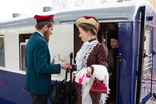Ekaterinburg, Russia - November, 30, 2018. Public performance for all passengers and guests of Ural railway - Chekhov's day. Conductor in costume and young woman in dress and hat leaving train. Historical reenactment