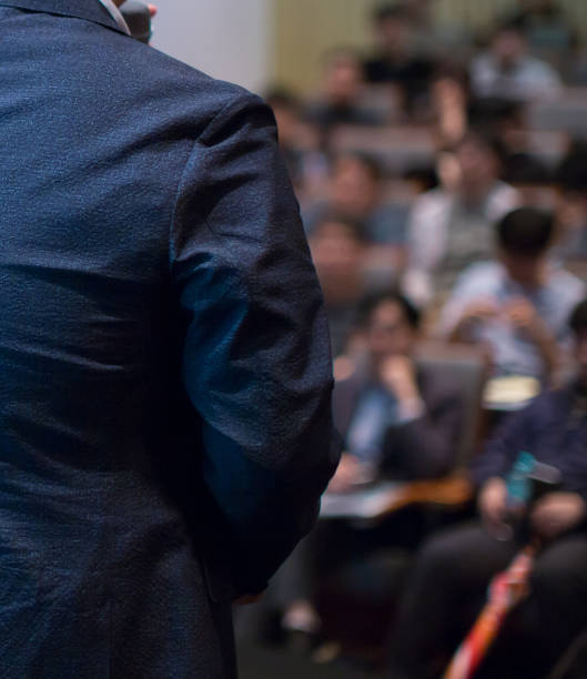 istock Conference photo audience and speaker giving speech. Seminar presenter on a panel during forum. Corporate manager in sales executive training discussion on stage. Investor pitch presentation. 1205667928