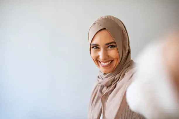 Muslim caucasian woman taking selfie. Happy beautiful woman with scarf take picture of her self using smartphone. A young beautiful and modern muslim woman taking selfie.