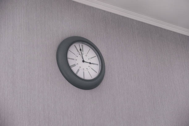 istock Round clock hanging on gray wall indoors. 1205683115