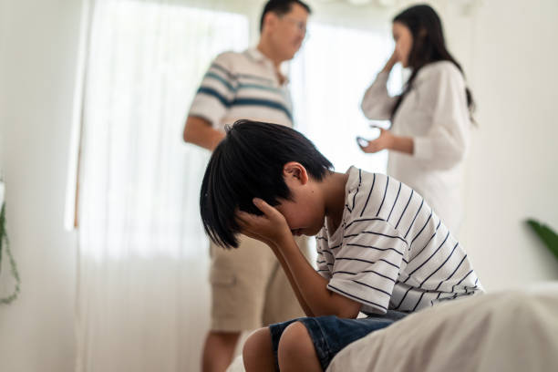 ragazzo asiatico ragazzo seduto e piangendo a letto mentre i genitori hanno litigato o litigare conflitto a casa. i bambini che coprono viso e occhi con le mani non vogliono vedere la violenza. problema domestico in famiglia. - wife father mother offspring foto e immagini stock