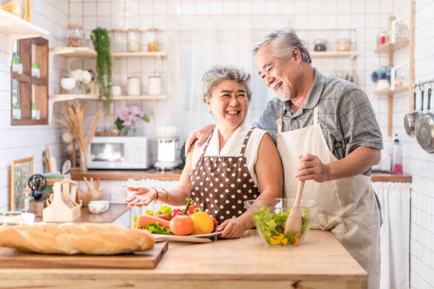 couple senior asian elder happy living in home kitchen. grandfather cooking salad dish with grandmother with happiness and smile enjoy retirement life together. older people relationship and activity. - retirement senior adult breakfast active seniors imagens e fotografias de stock