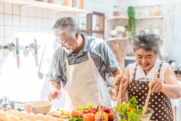 couple senior asian elder happy living in home kitchen. grandfather cooking salad dish with grandmother with happiness and smile enjoy retirement life together. older people relationship and lifestyle - cooking senior adult healthy lifestyle couple imagens e fotografias de stock