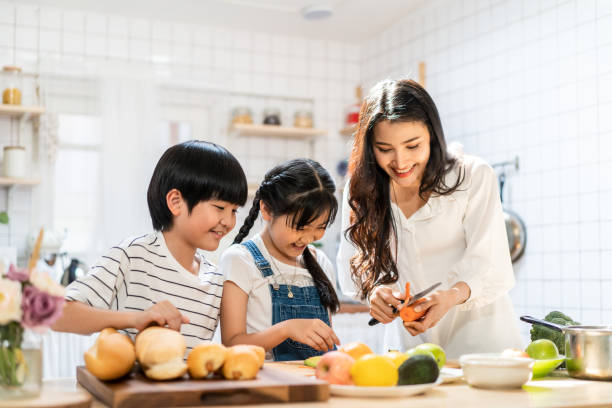 belle famille asiatique mignonne faisant la nourriture dans la cuisine à la maison. verticale de mère et d’enfants souriants restant au comptoir de cuisson préparant l’ingrédient pour le repas de dîner. activité familiale heureuse ensemble. - thai cuisine photos et images de collection