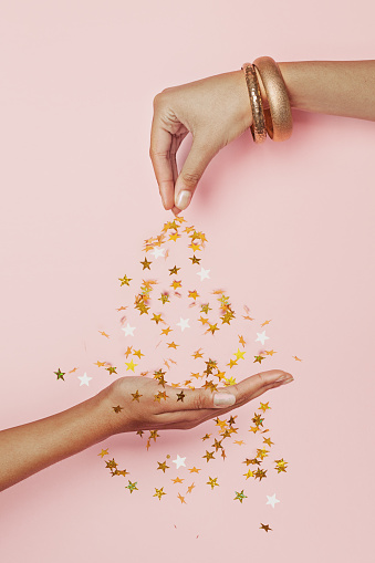 Female hand sprinkles gold confetti stars decoration on hand on pastel pink background. Celebration, Wedding, Christmas and Birthday party concept