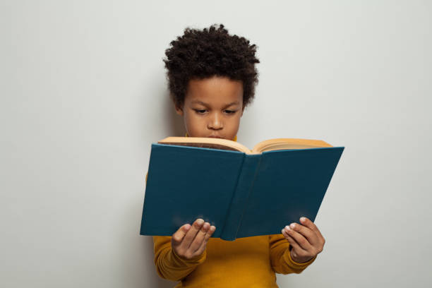 istock Serious black kid boy reading a book on white background 1205689094