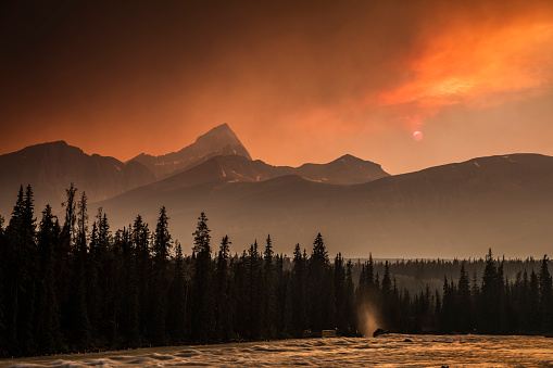 Moody sky over the Canadian Rocky Mountains in Banff National Park, Alberta Canada. The sun is shining through the red dust of forest fires in British Columbia. The particles in the air cause blue light to scatter, leaving longer-wavelength red light to shine through.