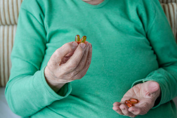 wrinkled hands of a senior person holding vitamin pills - vitamin pill picking up pill capsule imagens e fotografias de stock