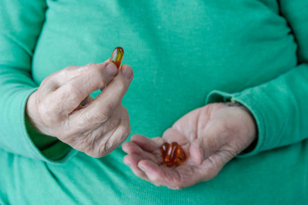 wrinkled hands of a senior person holding vitamin pills - vitamin pill picking up pill capsule imagens e fotografias de stock