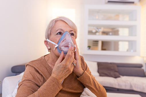 Sick elderly woman making inhalation, medicine is the best medicine. Ill senior woman wearing an oxygen mask and undergoing treatment. Senior woman with an inhaler