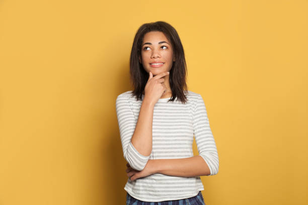 istock Happy young black woman student looking up and thinking on yellow background 1205692748