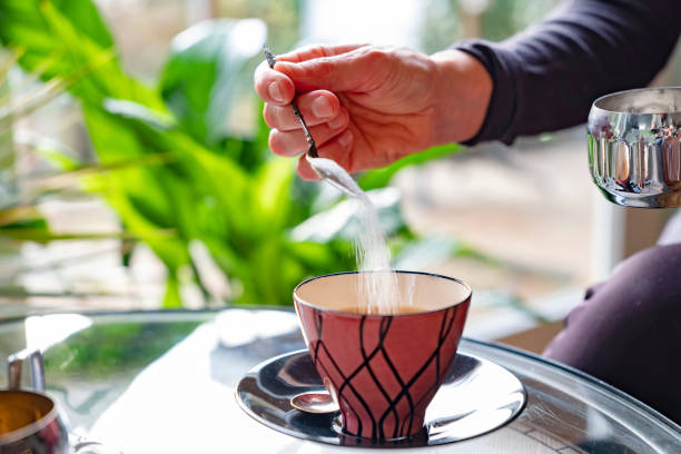 istock Women's hand does sugar in the pink retro tea cup, behind her a window through which the sun shines 1205699230